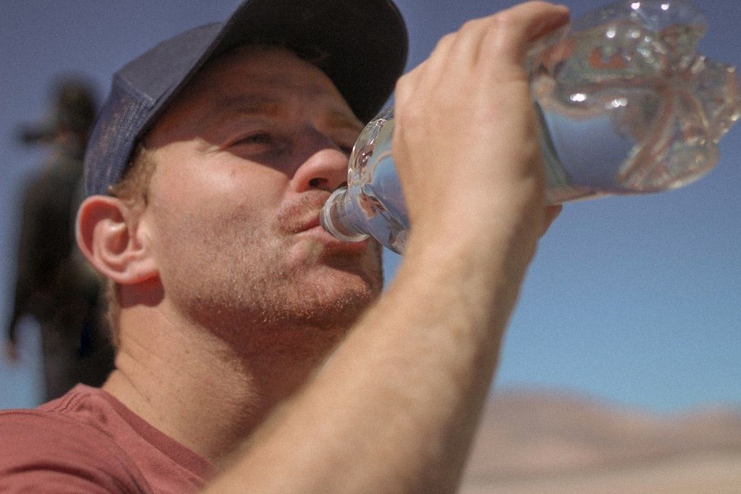Löpare i keps dricker vatten ur en genomskinlig flaska i solsken